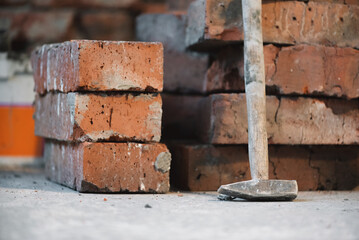 Stack of old bricks and hammer on the brick wall background.