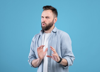 Disgusted young guy refusing something, gesturing NO or STOP over blue studio background