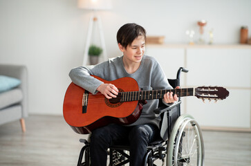 Handicapped teen boy in wheelchair playing guitar and singing indoors. Stay home hobbies