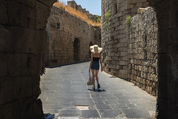 Tourist girl in a hat walks along a narrow city street in summer