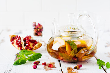 Fruit tea with berries, lemon, lime and mint leaves in glass teapot on white light wooden...
