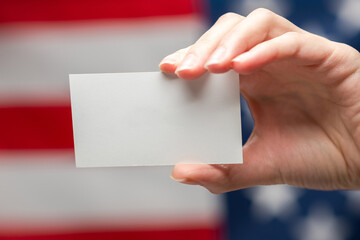 Obraz premium Empty card in woman hand. Copy space. American flag background.