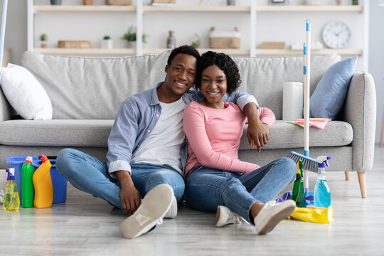 Tired black couple sitting on floor with cleaning tools