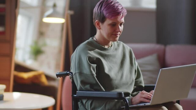 Young caucasian disabled woman on wheelchair using laptop while working online at home