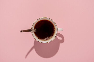 Mug of black coffee on a pink background. With a hard black shadow.