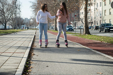 Two teenage girls rollerblading on an asphalt road
