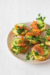 Delicious hearty appetizer, salmon toast on a white plate, round fried bun with red fish, cucumber, hollandaise sauce and pea sprouts