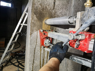 a worker works with a diamond drill on a machine fixed to the wall, drills a hole in the concrete for an electric cable and outlet with water supply