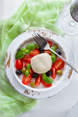 Mozzarella cheese salad plate with fresh tomatoes, black and green olives, basil. A glass of red wine, olive oil dressing.