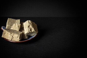 Pieces of sunflower halva on a saucer and a black background. Space for text