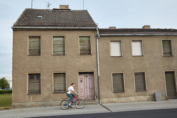 Old residential house with closed shalousies. Bicyclist rides from left to right. Man on bicycle is...