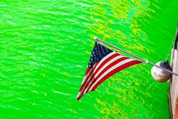 An American flag hangs down next to a life ring and buoy above the freshly dyed bright green river in downtown Chicago in 2021 making a great St. Patrick's Day holiday background.