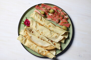 Pancakes on green plate with salty salmon slices, olives, rose flower on white table