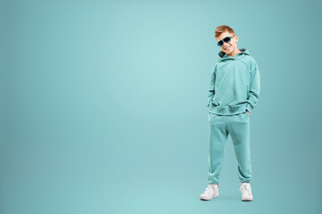 Little in a turquoise suit poses and fools around on a turquoise background, looks at the camera. Children's studio portrait. Childhood lifestyle concept.