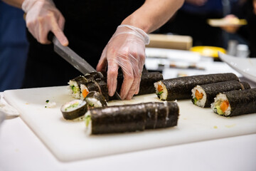 Chef en train de couper des morceaux de sushis dans un rouleau - obrazy, fototapety, plakaty