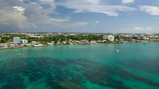 Drone shot over the ocean moving towards small Cayman Islands town