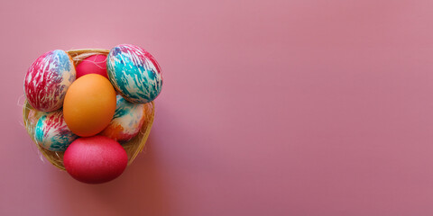 Happy Easter holiday! Colorful hand-painted Easter eggs in a decorative nest on pink background.