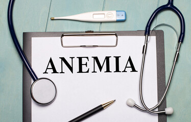 On a light blue wooden background, there is a paper labeled ANEMIA, a stethoscope, an electronic...