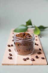 Body scrub from coffee in a glass jar on a light background on a wooden stand next to coffee beans and leaves, minimalism, vertical photo