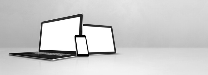 Laptop, mobile phone and digital tablet pc on white concrete office desk. Banner background