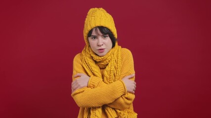 Sad sick ill short hairdo young woman 20s years old in yellow knitted sweater hat scarf looking camera rubs her hands frozen chills shivers cold season isolated on bright vivid red background studio
