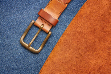 Brown leather belt with bronze buckle on chamois leather and jeans background texture. Casual man fashion concept. Top close up view.