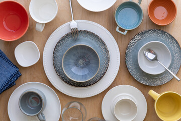 Wooden table set with many different empty plates, bowls and cups or glasses.