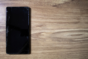 Broken phone on stall screen on wooden table. Smartphone with cracks on the screen.