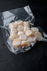 Frozen meat scallop in vacuum package, on black textured background