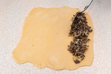 Yeast dough rolled out on the table, prepared for making patties with mushrooms, put on a metal spoon.