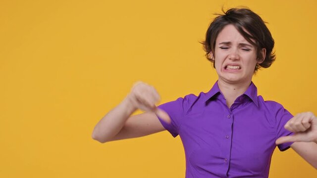 Disgusted abhorred shocked young woman 20s years old in violet shirt looking aside on workspace copy space mockup promo commercial area showing thumb down dislike isolated on yellow background studio