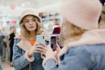 Pretty woman trying on a pink hat in the store making a selfie photo on the smartphone