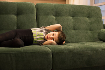 a baby boy lies resting with his arms folded on a green sofa at home