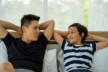 Asian young boy playing in white bed with father in new normal work from home