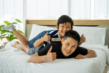 Asian young boy playing in white bed with father in new normal work from home