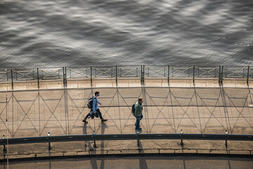 Fototapeta premium Prague, Czech republic - February 24, 2021. Two people walk on the pathway by Moldau river in sunset - one with mask, second without protection