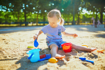 Adorable little girl having fun on playground in sandpit