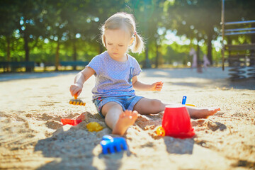 Adorable little girl having fun on playground in sandpit
