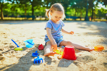 Adorable little girl having fun on playground in sandpit