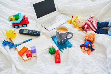 Obraz premium Laptop, cup of coffee, notebook, phone and different toys in bed on clean white linens