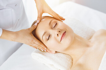 Beautiful caucasian woman enjoying facial massage with closed eyes in sunny spa salon. Relaxing treatment in medicine