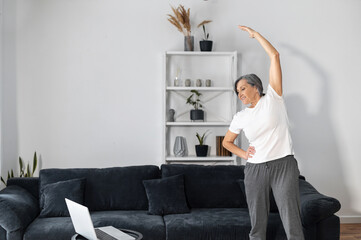 Active and sporty senior female warming out before workout at home, an older woman stretching arms...