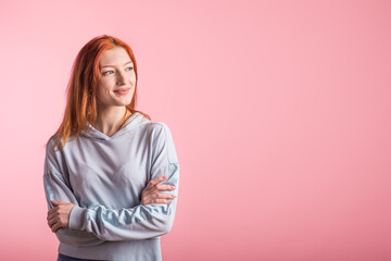 Smiling redhead girl with crossed arms in studio on pink background