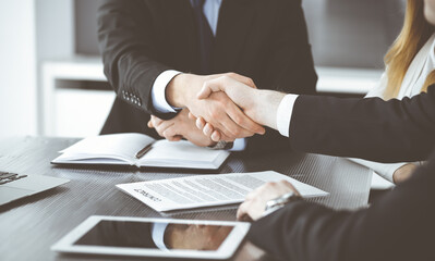 Unknown businessmen shaking hands above the glass desk in a modern office, close-up. Unknown business people at meeting. Teamwork, partnership and handshake concept