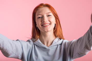 Redhead girl makes selfie in studio on pink background