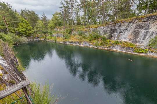 Beautiful nature landscape view of rain drops on pond surface. Ricky coast and tall pine trees on pale sky background. Sweden.