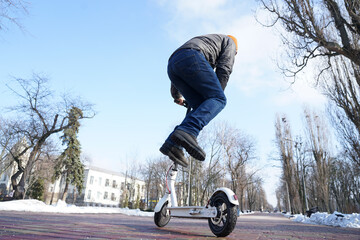 The guy rides and jump an electric scooter in the spring in the park.