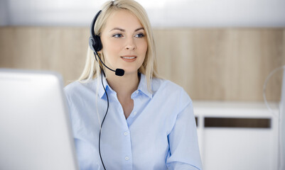 Blonde business woman sitting and communicated by headset in call center office. Concept of...