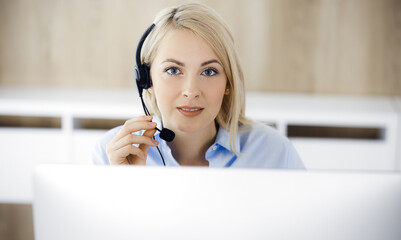 Blonde business woman sitting and communicated by headset in call center office. Concept of telesales business or home office occupation