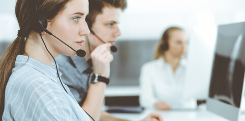 Fototapeta premium Call center. Group of casual dressed operators at work. Brunette business woman in headset at customer service office